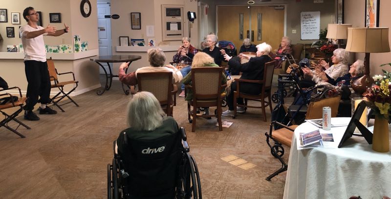 Group of people in assisted living community practice TaiChi is chairs, sitting in a common room