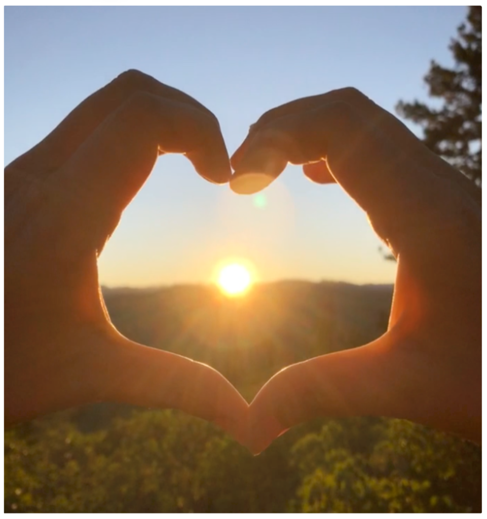 hands in a heart shape over the sun in the background