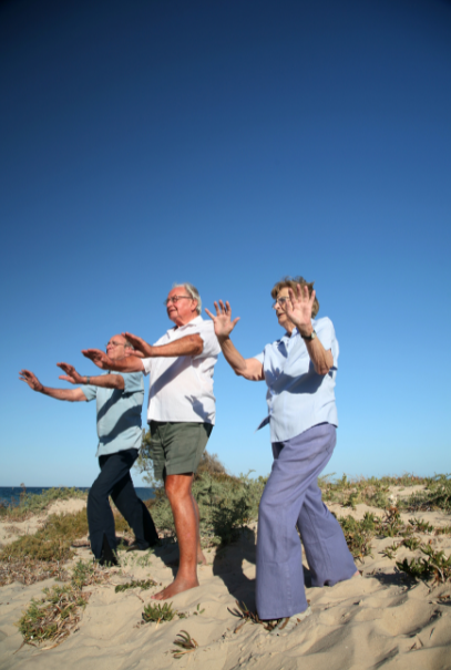 group of 3 older people practicing tai chi on the beach